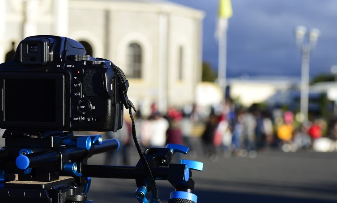 A digital camera mounted on a tripod, focused in the foreground with a people in a public space