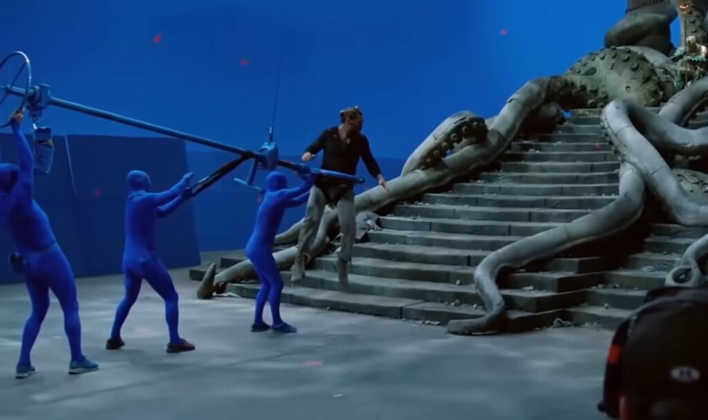 A man fights actors in blue suits on a prop staircase