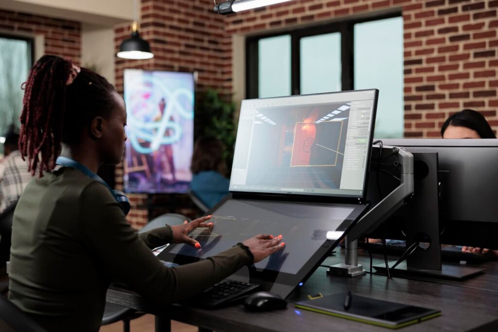 A girl sits at a computer and writes a project on a tablet